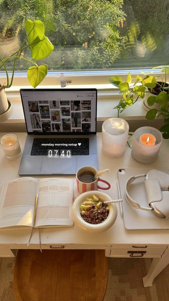 Cozy home office setup with a laptop, planner, coffee, and healthy breakfast by a window with plants. Perfect for a productive morning.