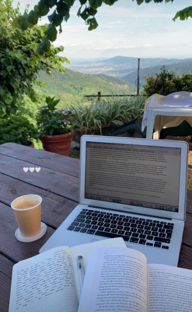 Laptop, notebook, and coffee cup on a table with a scenic mountain view, perfect setting for remote work or study retreat.