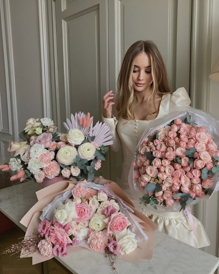 Woman in elegant cream dress with pink and white floral bouquets, featuring roses and ranunculus, in a luxurious setting.