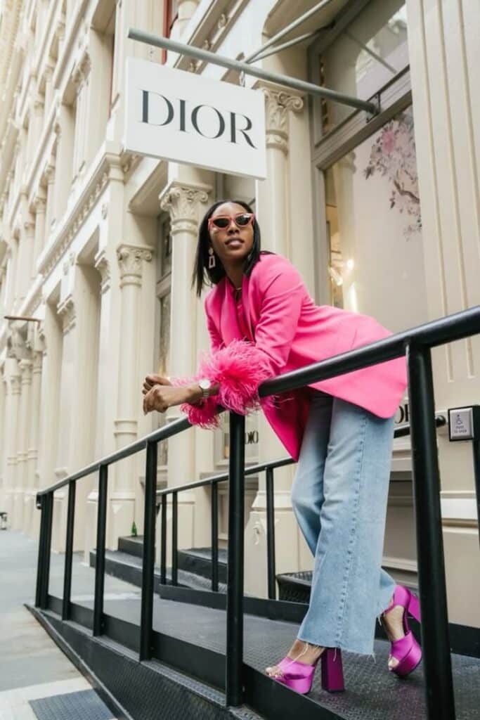 Stylish woman in a pink blazer and sunglasses poses confidently outside Dior store. Fashionable street style.