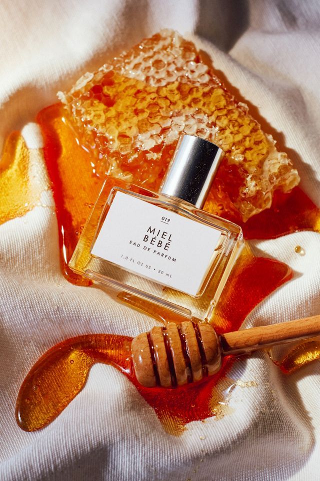 Perfume bottle with honeycomb, showcasing Miel Bébé Eau de Parfum, surrounded by dripping honey on fabric. Luxurious and sweet.