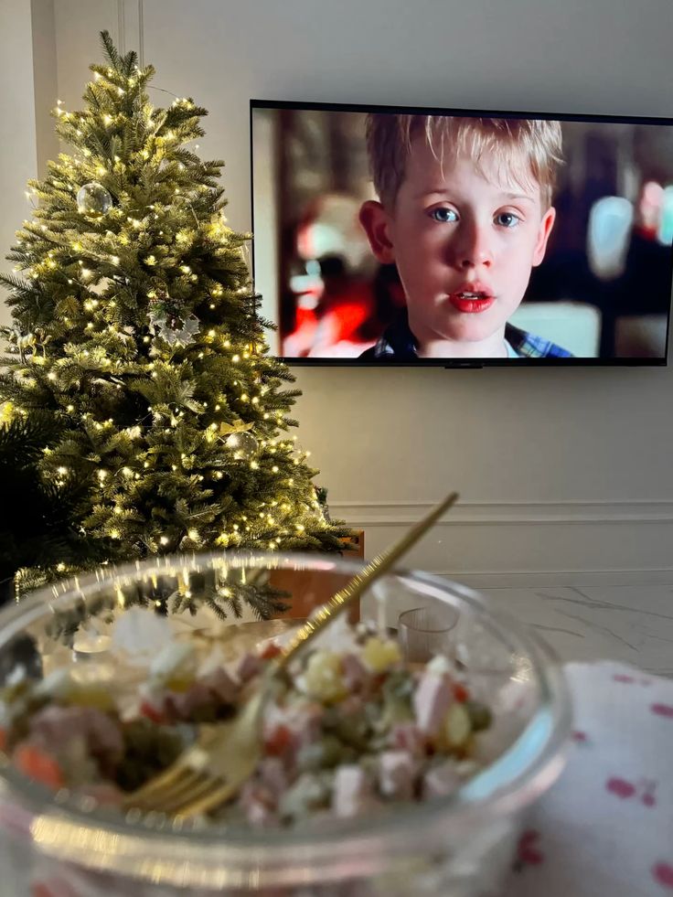 Festive Christmas scene with decorated tree, a holiday movie on TV, and a bowl of salad on the table. Cozy seasonal vibes.