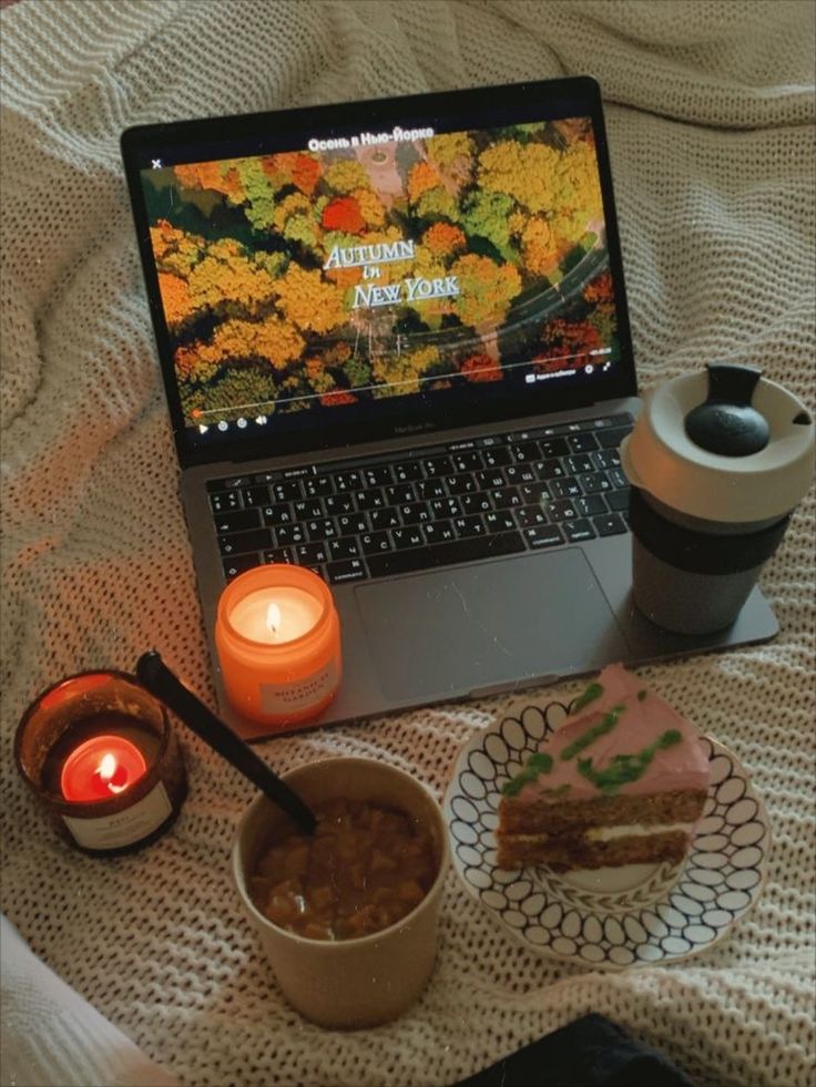 Cozy autumn setup: laptop playing a movie, coffee, candles, and cake on a knitted blanket. Perfect fall vibes for a relaxing day.