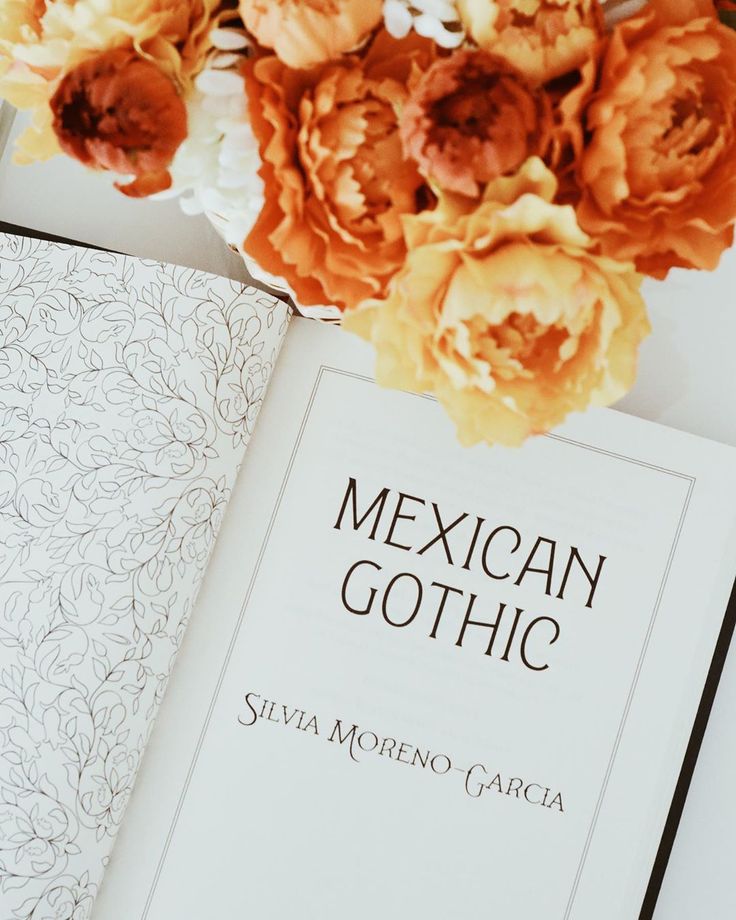 Open book titled Mexican Gothic with vibrant orange flowers nearby for an artistic touch.
