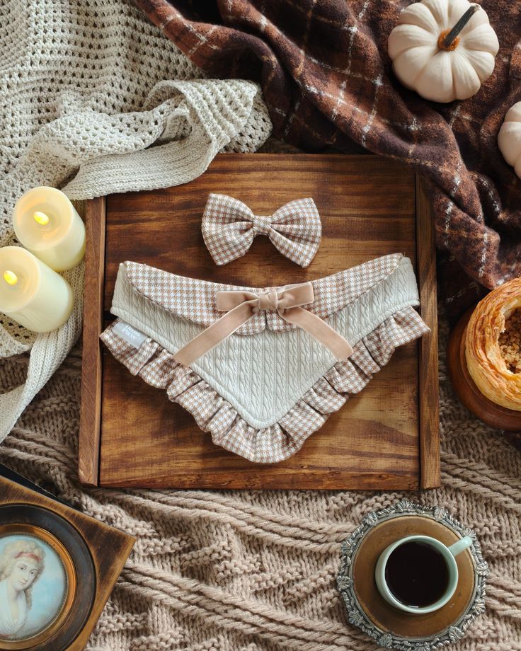 Cozy fall setup with a plaid baby outfit and bow, candles, pumpkins, coffee, and knitted textures for a warm seasonal vibe.