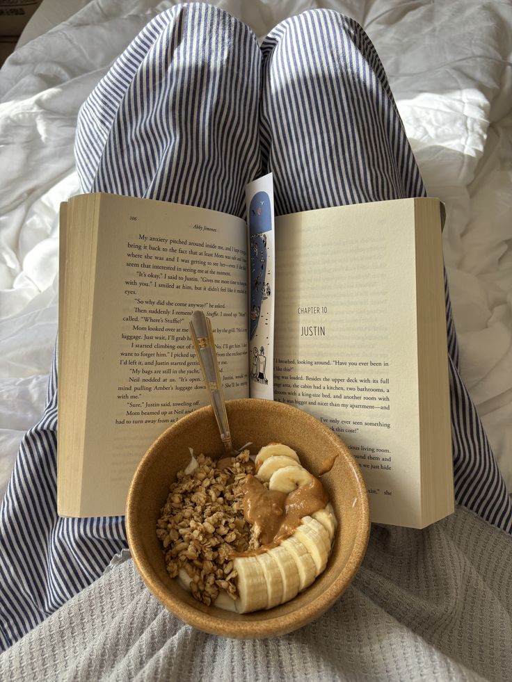 Cozy morning with a yogurt bowl, granola, bananas, and peanut butter. Pajamas, open book, and natural light complete the serene scene.