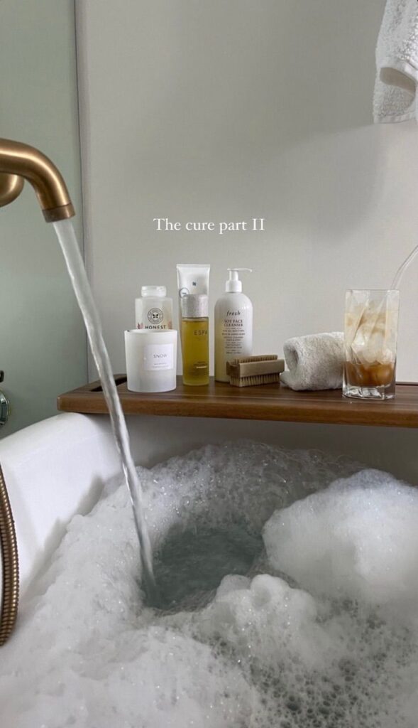 Luxurious bubble bath with flowing water, self-care products, and a drink on a bath tray for ultimate relaxation.
