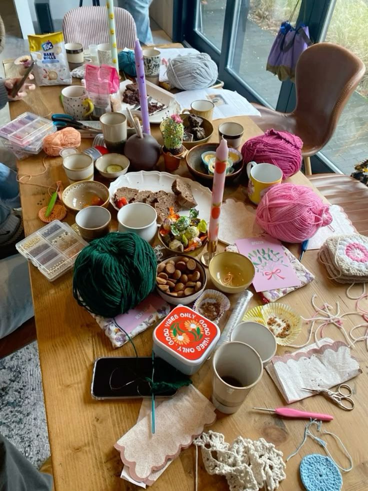 Cozy craft session with yarn, crochet tools, snacks, and drinks on a wooden table. Perfect for a creative afternoon.
