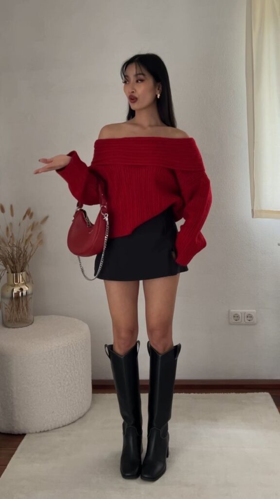15aafa3f-7738-44b9-a3fc-c5980fa6d78b - Handy Home Woman in off-shoulder red sweater and black skirt poses stylishly with a red handbag, accented by black knee-high boots.