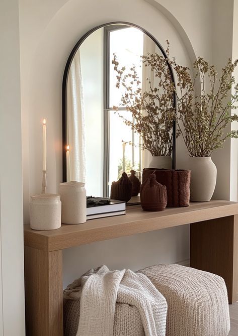 Modern entryway decor with a wooden console table, arched mirror, dried flowers, candles, and cozy knit throws for a warm ambiance.
