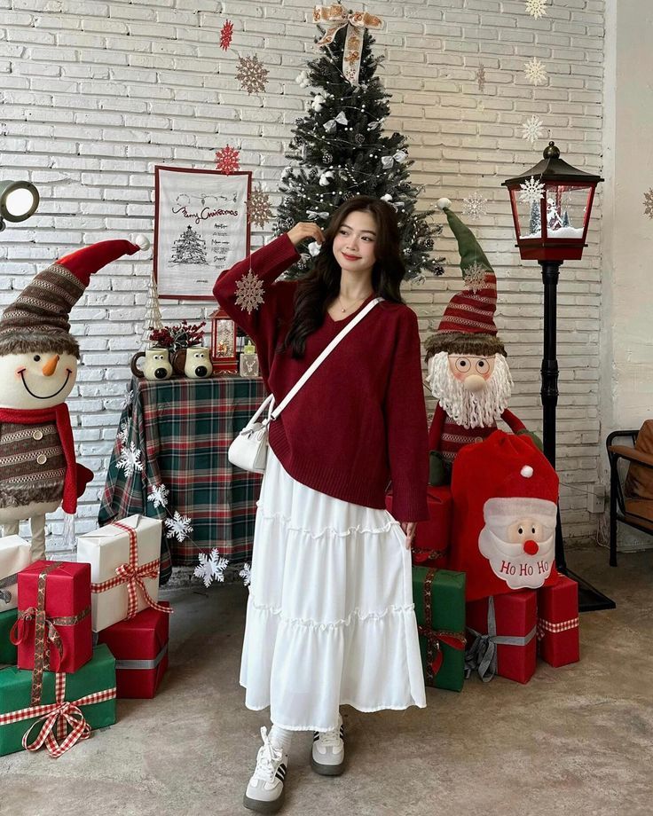 19 Classy Cozy Korean Christmas Outfit Ideas - Handy Home Festive scene with a woman in a red sweater and white dress, standing by Christmas tree and decorations. Holiday spirit.