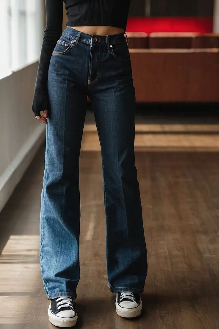Person wearing high-waisted jeans, black crop top, and sneakers in a stylish indoor setting. Fashionable casual outfit.