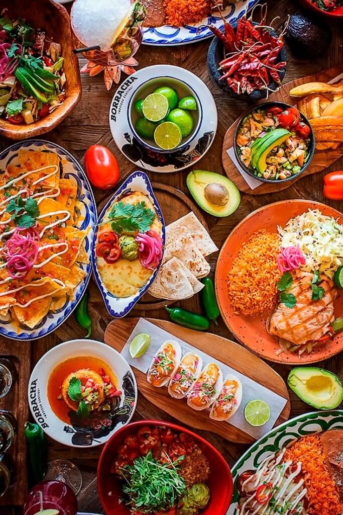 19 Receitas de Comida Mexicana Típica Simples e Fácil_ Saiba Como Fazer - Handy Home Assorted Mexican dishes on table with tacos, nachos, rice, guacamole, and fresh lime slices—vibrant and colorful fiesta spread.