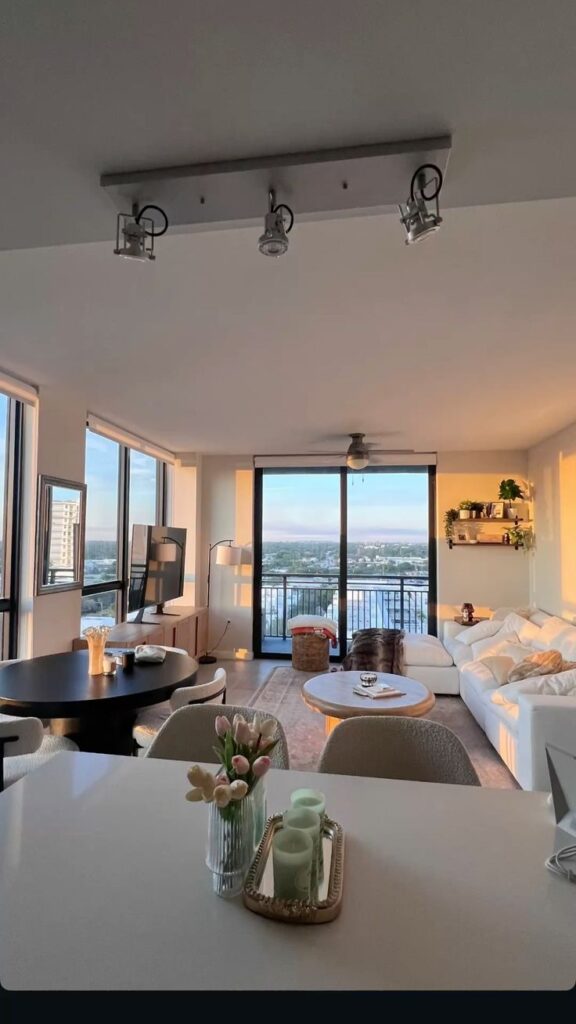 Modern living room with large windows, cozy decor, and a scenic city view at sunset. Bright and inviting interior design.