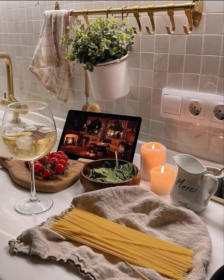 Cozy kitchen setup with pasta, wine, and fresh ingredients. Candles and a tablet create a relaxing ambiance for cooking.