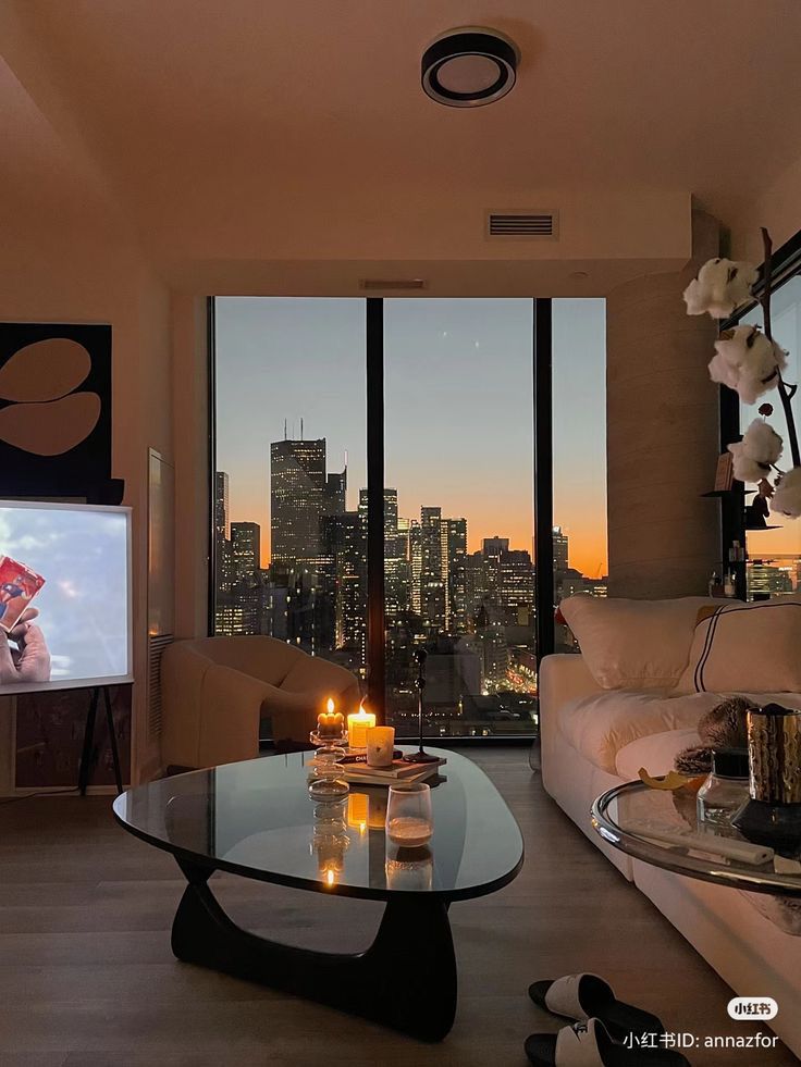 Cozy living room with candles on the table, large window view of city skyline at sunset, and a couch, perfect for relaxation.