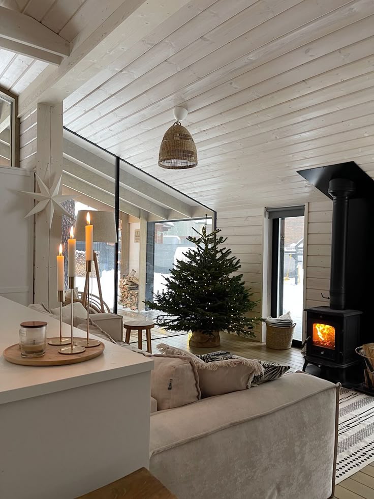 Cozy Scandinavian living room with Christmas tree, candles, and wood stove, creating a warm holiday atmosphere in a bright space.