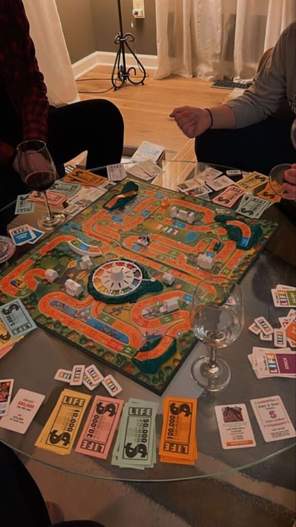 Friends playing the Game of Life board game with drinks on a cozy evening.