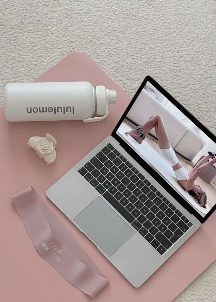 4ce6602b-b9a6-4a59-9fb5-20d7a782e376 - Handy Home Laptop streaming a workout on a pink mat with a water bottle and resistance band, ideal for home fitness routines.