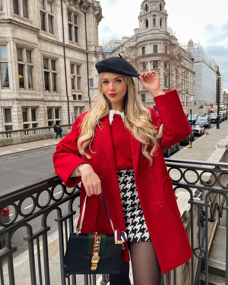 53b51562-c593-4903-9c80-6245b63715fe - Handy Home Woman in chic red coat and beret in urban setting, holding a stylish handbag, with historic architecture in the background.