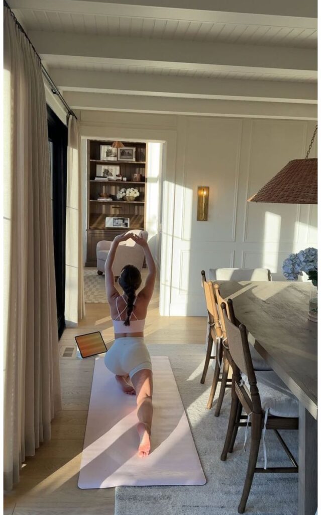 Woman practicing yoga in a sunlit room, following a virtual class on a tablet. Serene home workout environment.