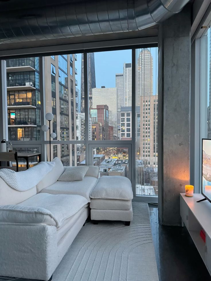 Modern apartment living room with plush sofa, cityscape views through large windows, ambient lighting, and sleek decor.
