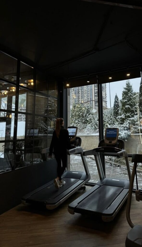 Woman jogging on a treadmill in a gym with a snowy cityscape view from large windows. Fitness, workout, winter scenery.