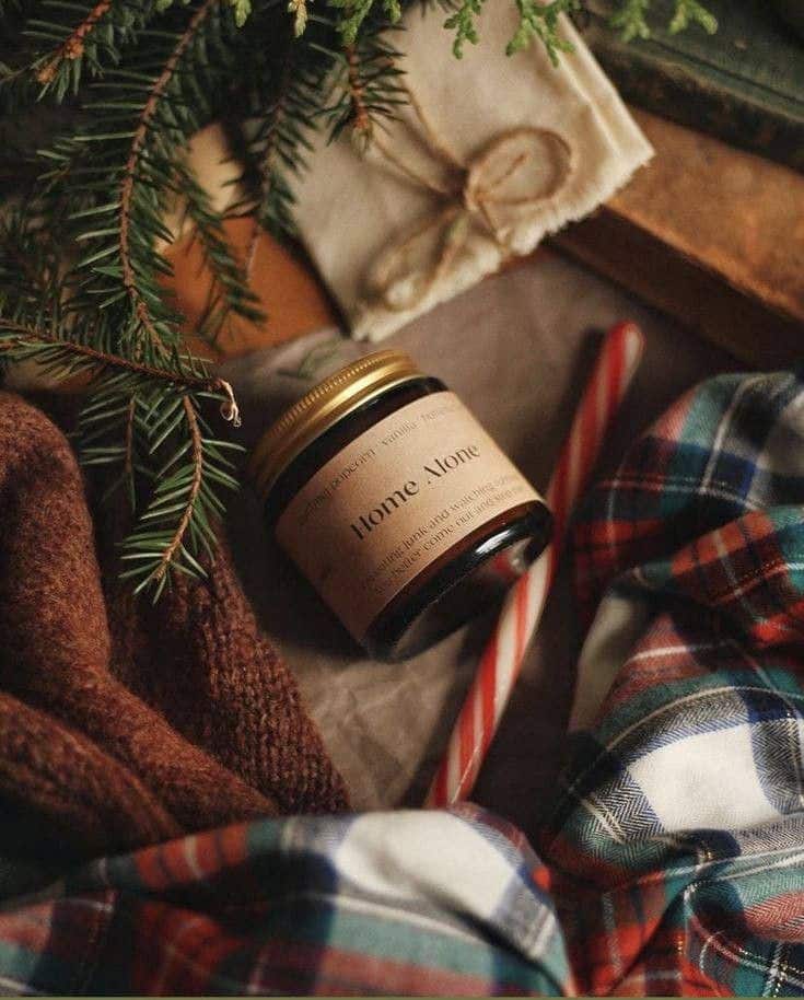 Cozy candle setting with pine branches, a candy cane, and plaid fabric, perfect for holiday warmth and comfort.