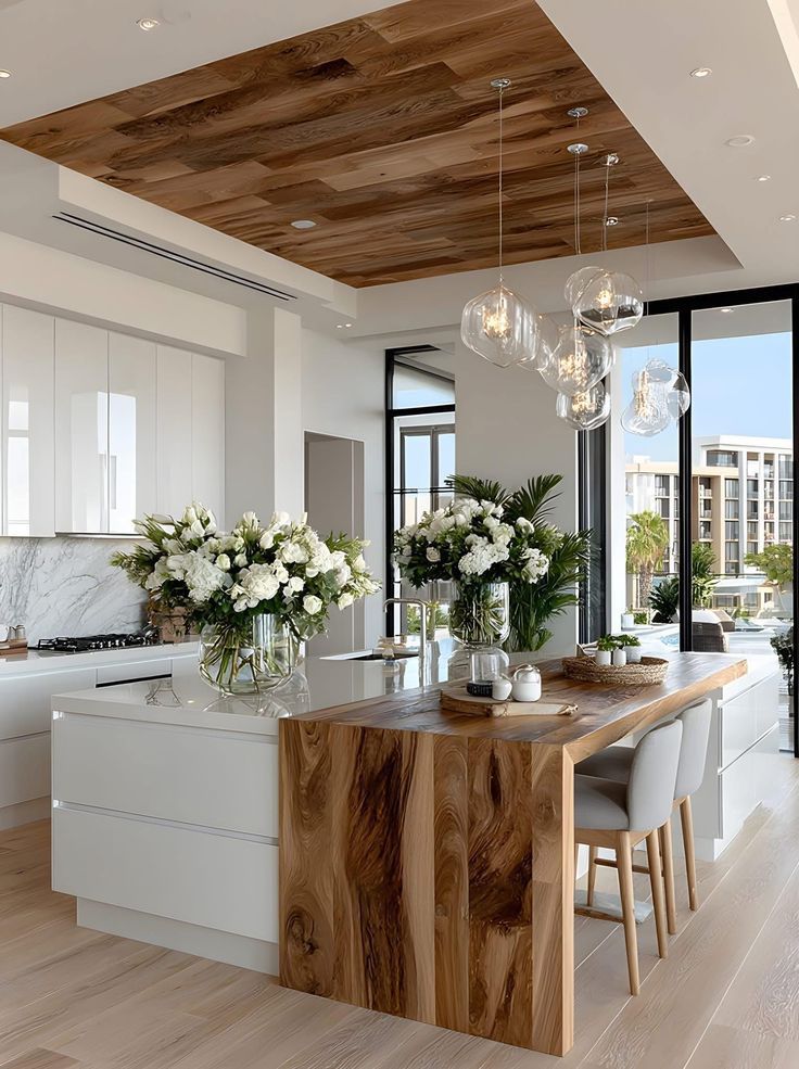 Modern kitchen with wood accents, white cabinetry, marble backsplash, and elegant pendant lighting, featuring floral centerpieces.