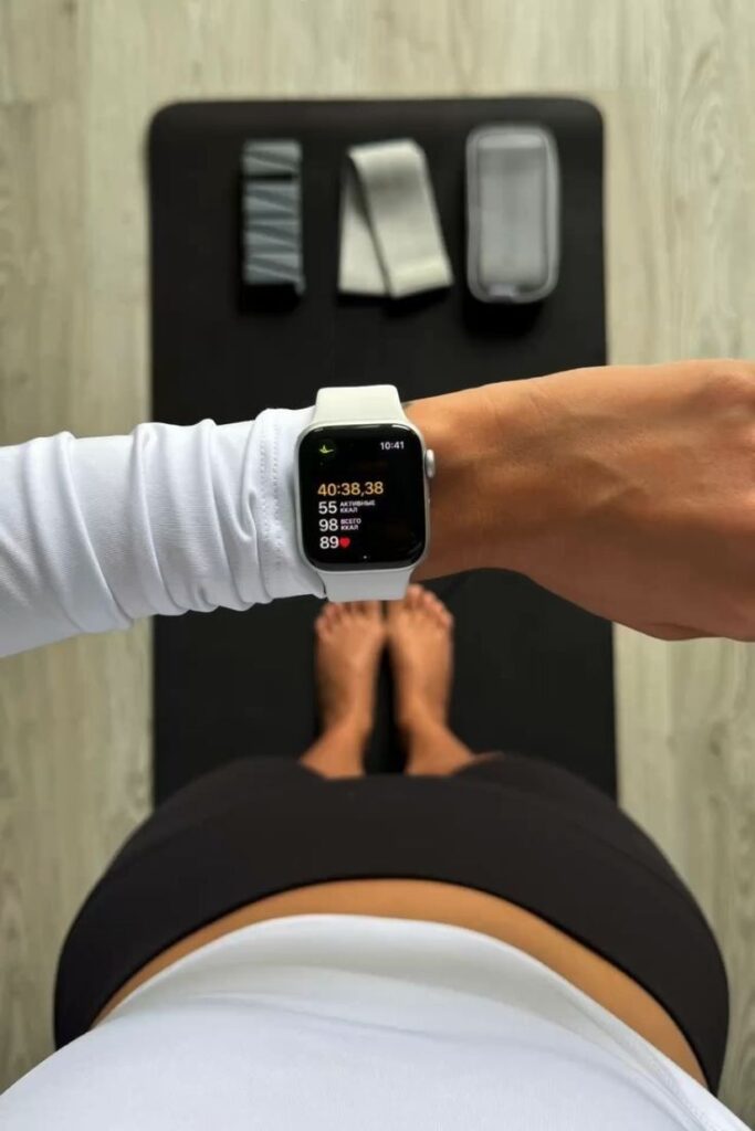Person wearing a smartwatch displays workout stats, standing on yoga mat with exercise bands. Fitness and wellness concept.