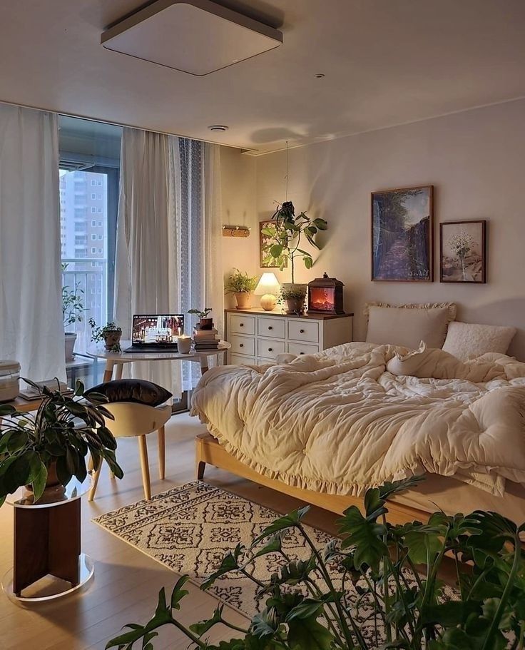 Cozy bedroom with plants, warm lighting, and neutral decor. Features a comfy bed, wooden furniture, and a small rug.