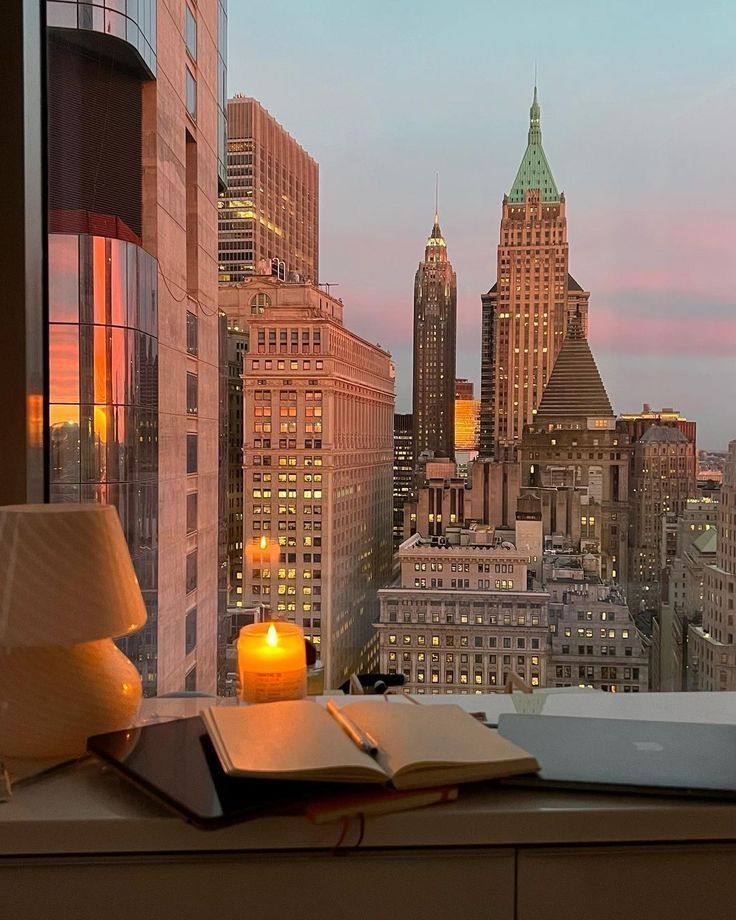 Cozy workspace with candlelit ambiance overlooking a stunning urban skyline at sunset. Calm and inspiring city view.