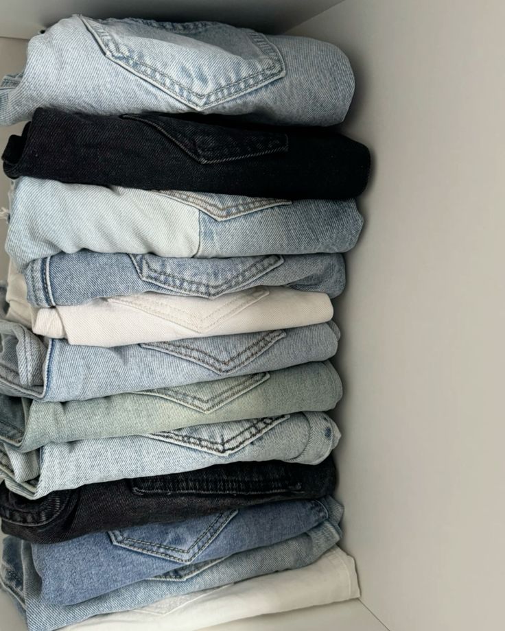 Stack of neatly folded jeans in various colors and shades, organized in a closet for easy access and stylish wardrobe management.