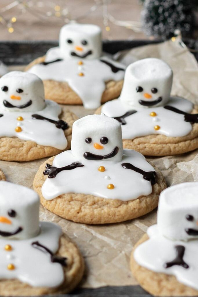 92d58d19-4be6-4b74-9092-e043b5c2b7d3 - Handy Home Melted snowman cookies with marshmallow heads and icing bodies on parchment paper, perfect for festive winter treats.