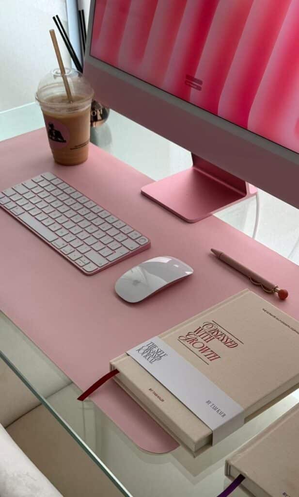 Modern pink workspace with desktop computer, keyboard, mouse, coffee, and notebooks. Perfect setup for creativity and productivity.