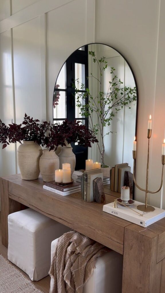 Elegant console table with candles, vases, and books, styled with a mirror and greenery for a chic and cozy home decor vibe.