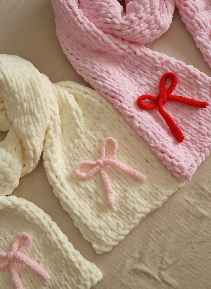 Soft knitted scarves in pink and cream with decorative bows, perfect for a cozy and stylish winter accessory.