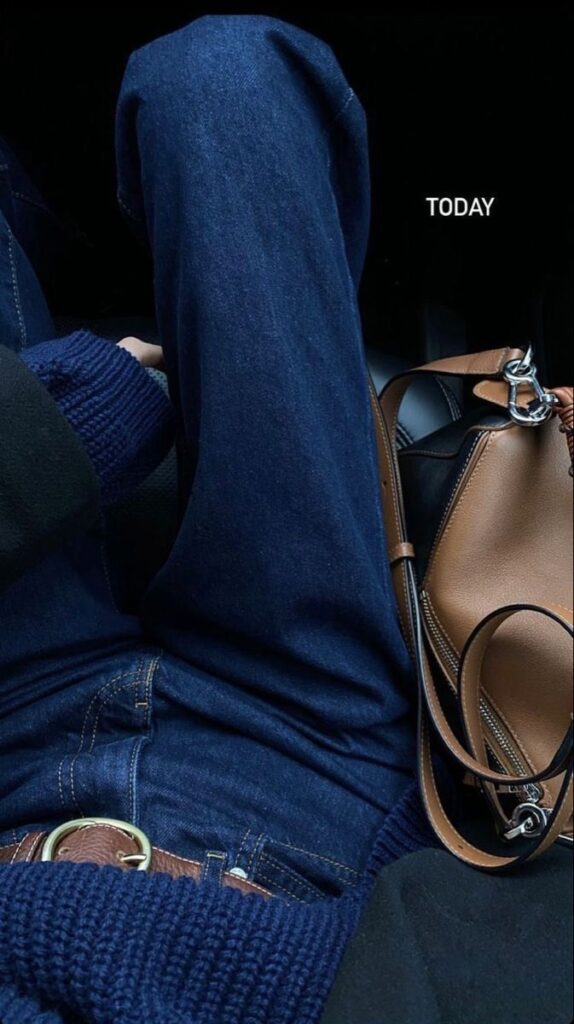 Casual outfit with blue jeans and sweater, paired with a brown leather bag, showcasing a relaxed, stylish look.
