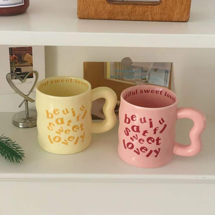 Colorful mugs with heart-shaped handles and playful text sit on a shelf, adding charm to a cozy kitchen or living space.