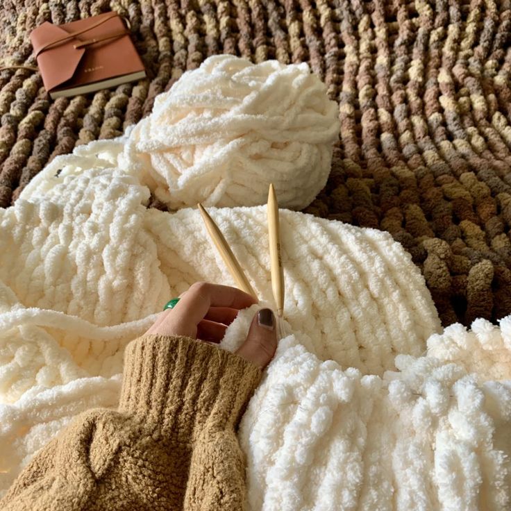 Best Affordable Indoor Autumn Activities - Handy Home Cozy knitting setup with soft cream yarn, wooden needles, and a notebook on a textured brown blanket.