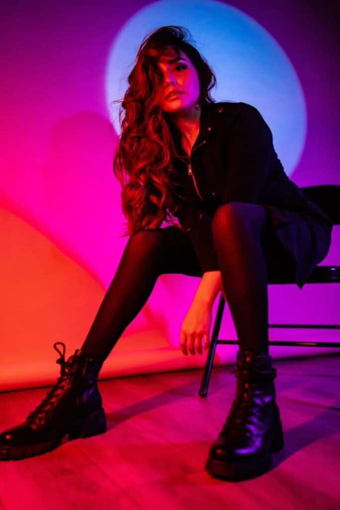 Bold Colors - Editorial Photoshoot - Handy Home Stylish person in edgy black outfit with boots, sitting in colorful red and blue lighting.