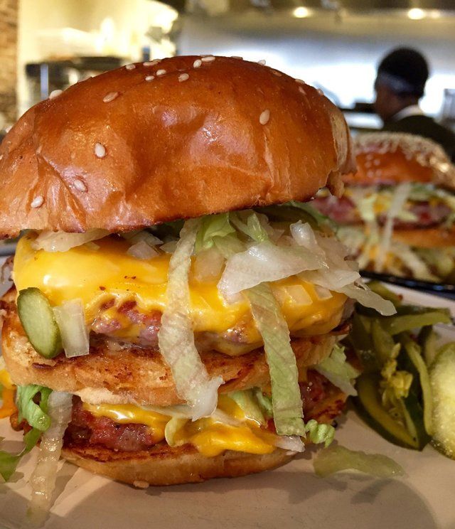 Boozy Hot Sauce Is About to Be Your New Obsession - Handy Home Juicy double cheeseburger with lettuce and pickles on a sesame bun, perfect for a delicious meal.