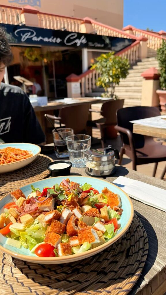 Caesar Salad 🥗 - Handy Home Fresh chicken salad and pasta at a sunny outdoor cafe, near steps with vibrant greenery.