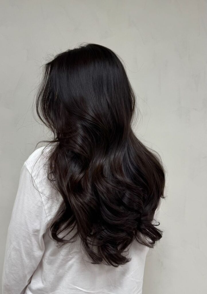 Care for your hair with the right brush - Handy Home Woman with long, wavy dark hair, wearing a white shirt, showcasing voluminous and healthy hairstyle against a neutral background.