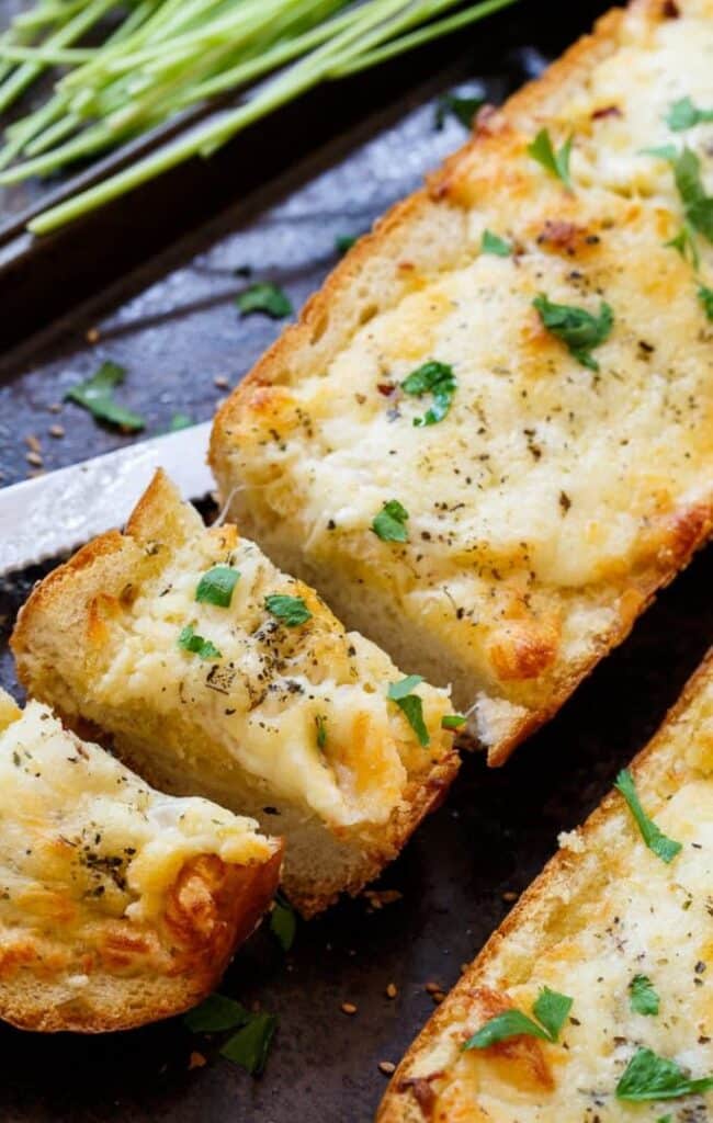 Cheesy Garlic Bread - Handy Home Delicious garlic cheese bread topped with herbs and fresh parsley slices on a tray, perfect for a savory snack or appetizer.