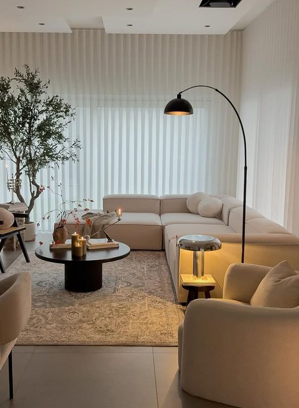 Modern living room with white sectional sofa, floor lamp, coffee table, elegant decor, and natural light through sheer curtains.