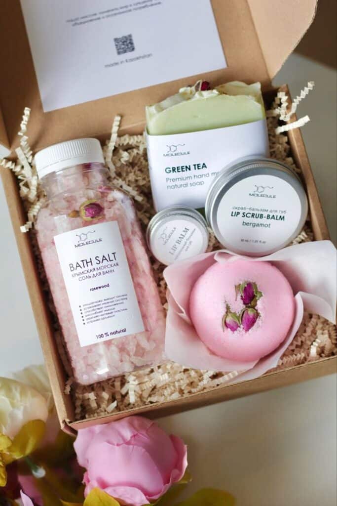 Gift box with bath salt, green tea soap, lip scrub, and pink bath bomb adorned with roses, ideal for relaxation and pampering.