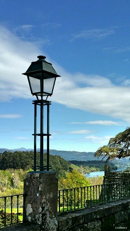 Farola Monçao Portugal - Handy Home Vintage street lamp against a scenic countryside backdrop with trees, river, and blue sky. Ideal nature and landscape view.