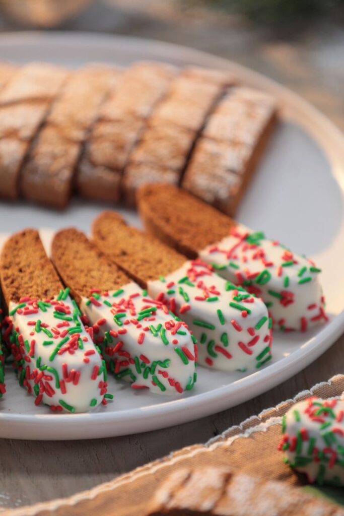 Gingerbread Biscotti Recipe - Handy Home Festive biscotti dipped in white chocolate with red and green sprinkles on a plate, perfect for holiday treats.