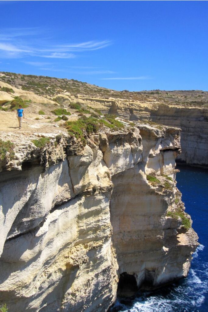 Gozo Malta - Handy Home Person walking along stunning cliff edge with blue sky and sea, rocky landscape, daytime.